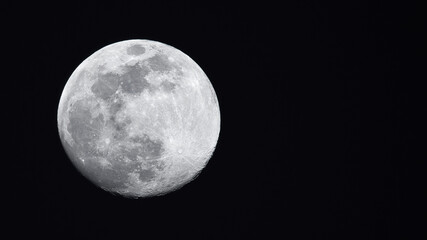 Horizontal photo of full moon showing meteor craters on a black background with copy space