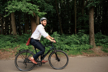 Dark haired businessman on bike, riding along park area outdoor.