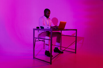 Fototapeta premium A man is sitting at a desk. A black programmer works using a laptop computer. the man works at night.