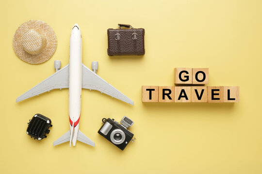 Flatlay picture of plane miniature, toy luggage, camera and hat with Go Travel wooden block.