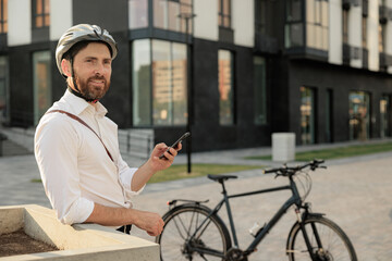 Smiling male entrepreneur with parked bike checking phone on street.