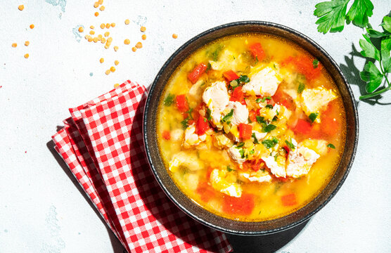 Warming autumn soup with red lentils, chicken fillet, vegetables, spices and paprika, comfort food. White table, hard light with leaf shadows, top view