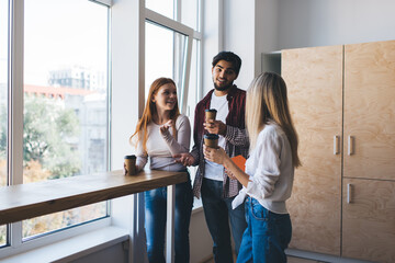 Group of colleagues standing with coffee cups near window in office