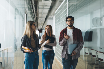 Positive multiracial colleagues communicating while standing in office hallway