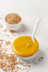 Mustard sauce in a bowl and seeds on a bright background.