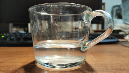 Glass mug with computer, monitor and keyboard in background on work desk. Close-up yellow mug. Home office