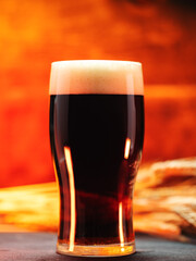 A glass of dark beer on a wooden table with ears of wheat. Back light