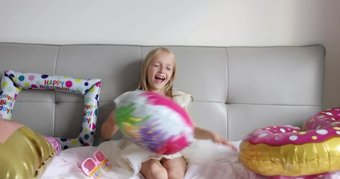 Indoor shot of pretty joyful cute adorable girl kid celebrating eight years old birthday with bright and colorful balloons, wearing casual fashionable dress. Kid having fun. Slow motion