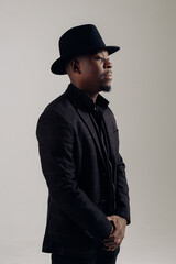Young african man in suit and hat stands against gray background.