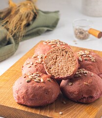 Rye and wheat flour bread buns with beetroot puree and sunflower seeds on a wooden board on a light concrete background. Baking bread with the addition of vegetable puree.