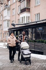 Happy interracial family walk on street and push baby carriage.