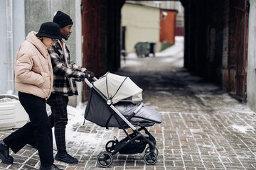 Happy interracial family walk on street and push baby carriage.