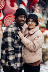 Portrait of young interracial couple at Christmas fair against background of decorations.