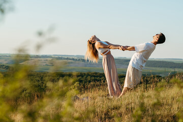 Young Adult Couple Holding by Hands, Man and Woman Practicing Yoga Outdoors with Scenic Landscape on the Background at Sunset
