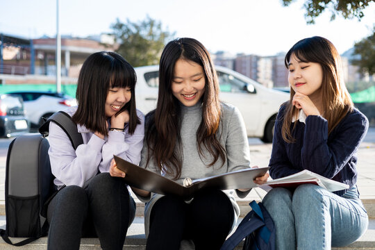 Group of Asian girls outdoor students.3 Women are sitting on a step of the street studying, the girl in the middle is the one who has the book. Education, friendship and concept of people.