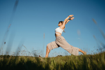 Young Woman Practicing Yoga Outdoors in the Field with Blue Sky on the Background