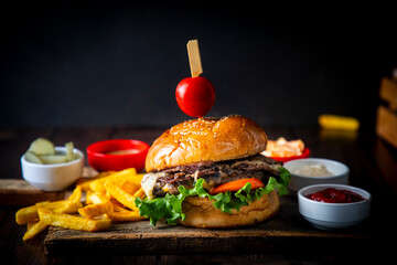 Homemade hamburger served with french fries. It looks delicious prepared with onions, hamburger patties, cheddar cheese and ham.