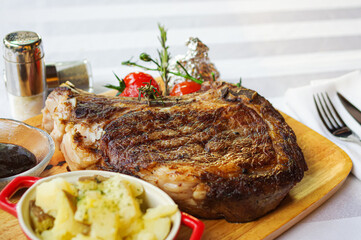 thick grilled bone-in steak ribeye with tomato and mashed potato on wood tray