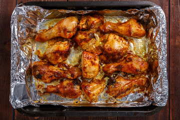 Baked chicken in sauce and herbs on foil on a baking sheet.