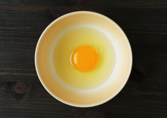 Top View of a Fresh Raw Egg Yolk and White in a Bowl Isolated on Wooden Table	