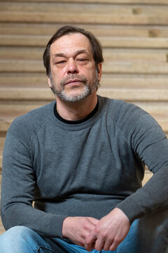 An Elderly Man Of 45-50 Years Old With Gray In His Beard Is Sitting On The Stairs.