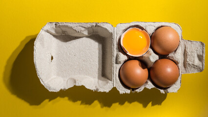 fresh raw eggs in the box on yellow background. Uncooked yolk in egg carton. Paper packaging for...
