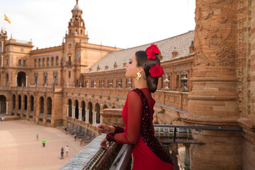 Beautiful teenage woman dancing flamenco on the balcony of a square in Seville. She wears a red...