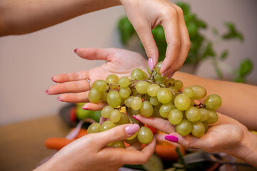Close-up on the hands of two women handing each other a bunch of grapes