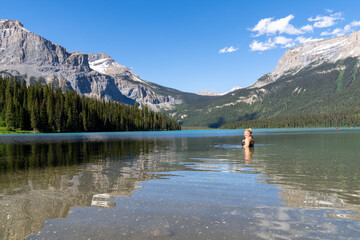 Fototapeta na wymiar Happy blonde woman swims in Emerald Lake in Yoho National Park, British Columbia on a sunny summer day
