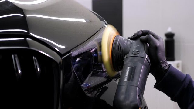 Car care in a modern car dealership, a worker polishes the black body. Polishing machine.