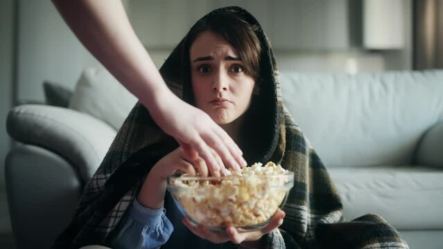 Camera view of addicted focused young woman watching interesting TV program film movie while her boyfriend try to steal her popcorn snack Greedy girl does not want to share her food and chase away him