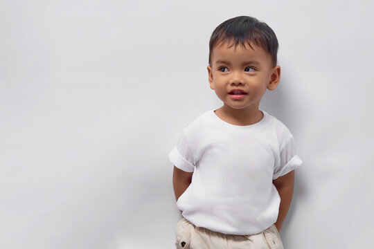 Smiling toddler Asian kid boy wearing white t-shirt standing with confidence and looking at empty space isolated on white background