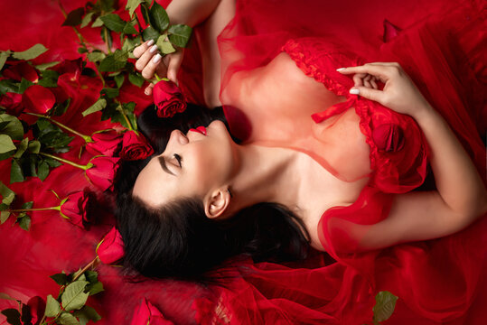 beautiful brunette woman lies surrounded by red roses and petals. She's wearing a red corset. Valentine's Day concept