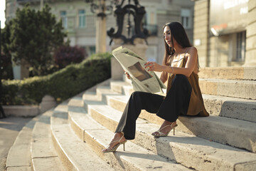 young woman reading a newspaper on the entrance steps of a building