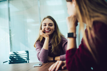Cheerful women sitting together at wooden table in office room