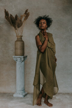 full body portrait of African American Canadian woman with afro wearing green toga next to roman column