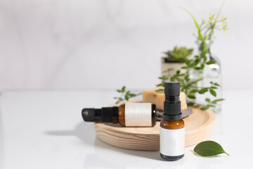 Fototapeta na wymiar Mockup of amber colored glass bottles of cosmetic and facial skincare product, on a wooden tray with branches and green leaves