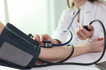 Doctor uses sphygmomanometer with stethoscope to check blood pressure of patient in hospital.