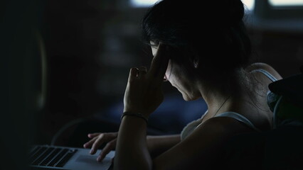 Woman working late at night in front of computer. Glowing light on person face staring at laptop screen at home