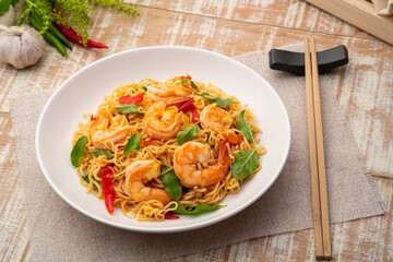 Spicy stir fried instant noodle with shrimps and thai basil leaves in white plate