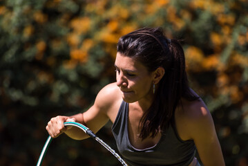 young and beautiful woman drinking water from the hose, after exercising, thirsty, sunny hot day