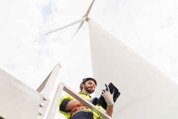 Male engineer working with plan inspecting or maintenance of wind turbines at windmill field farm. Male engineer using computer tablet control or monitoring wind turbine system at wind turbines farm © amorn