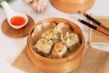 Traditional chinnese steamed dumplings Dim Sums in bamboo steamer with sauce and chopsticks on light surface. Asian food background. 