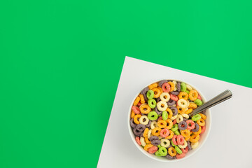 Colored breakfast cereal in a bowl on a green background, flat lay, children's healthy breakfast, copy space.