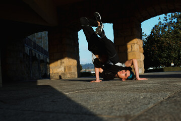 teenager boy with blue hair and sportswear dancing breakdace on the street. hip hop culture. street dancer doing pirouettes and stunts. © Alberto