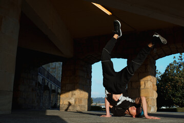 teenager boy with blue hair and sportswear dancing breakdace on the street. hip hop culture. street dancer doing pirouettes and stunts. © Alberto