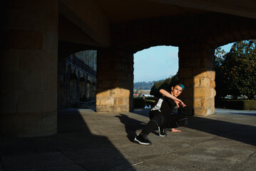 teenager boy with blue hair and sportswear dancing breakdace on the street. hip hop culture. street dancer doing pirouettes and stunts. © Alberto