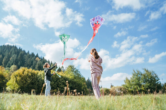 Girl and boy brother with flying colorful kites on the high green grass meadow in the mountain fields. Happy childhood moments or outdoor time spending concept image