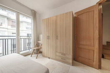 bedroom with oak wardrobe, balcony with large glass doors and white aluminum, access door of the same material and cream marble floor