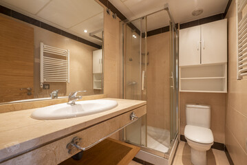 Conventional bathroom with marble countertop, square shower cabin with sliding glass partitions, large mirror embedded in the wall and white wooden cabinet